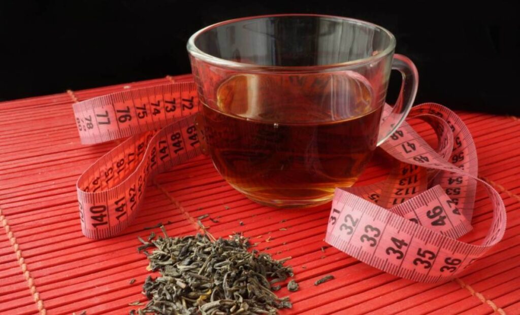 Čaj od peršuna u staklenoj šolji. Na stolu su i sušeni listići peršuna i krojački santimetar za merenje obima.