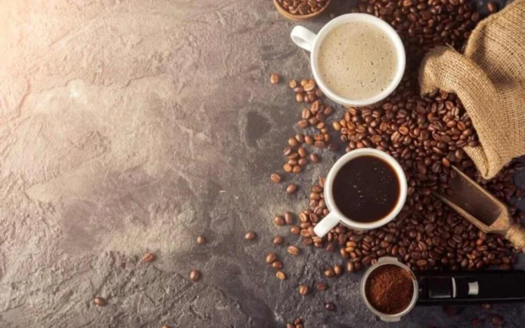 Šolja kafe se penom i bez pene, na kamenoj podlozi po kojoj su posuta cela zrna kafe