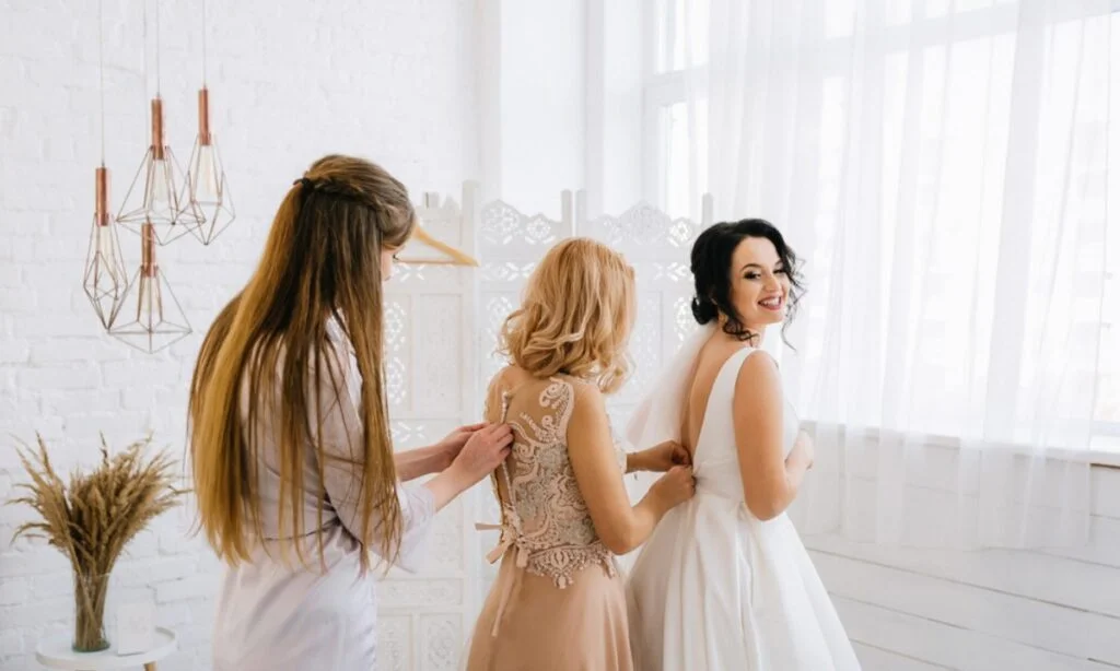 Kuma pomaže mladi da obuče venčanu haljinu, dok kumi pomaža drugarica u isto vreme.