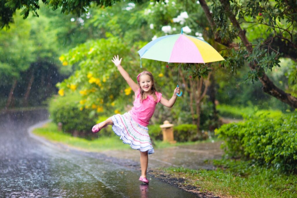 Devojcica drži visoko kišobran i podignutu nogu,k ao balerina, na kiši