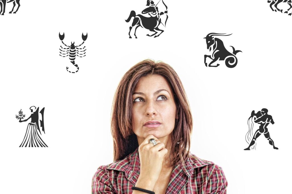 Žena koja drži ruku na bradi i razmišlja. U pozadini se vide ilustracije zodjačkih znakova.
