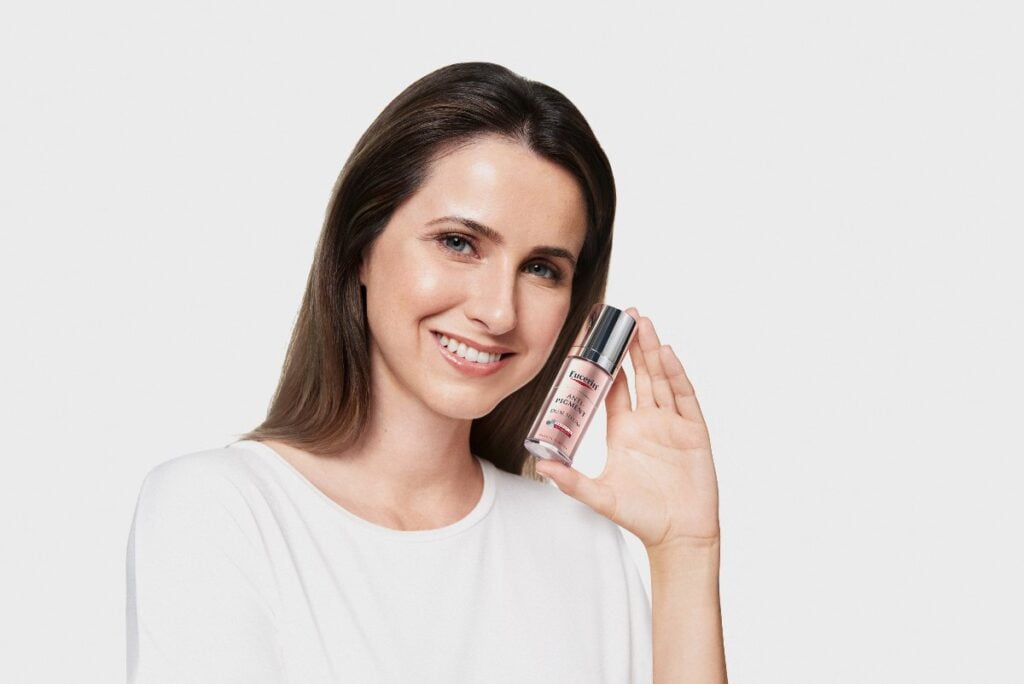 Smeđokosa žena, nasmejana drži u ruci flašicu seruma za tretiranje hiperpigmentacija