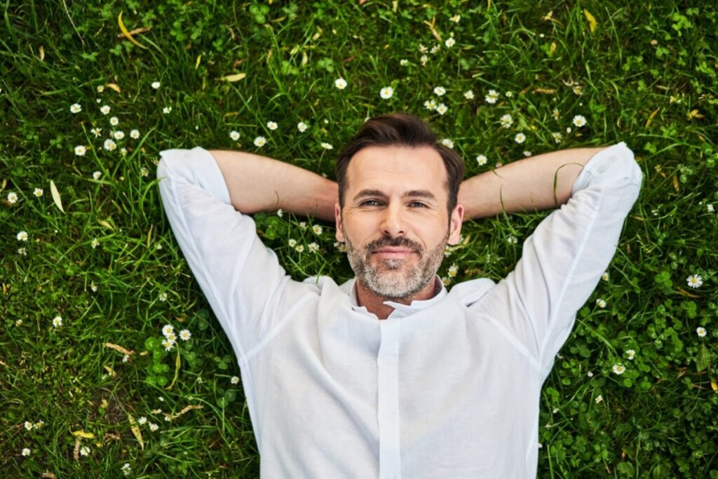 Zadovoljan, sredovečni muškarac u beloj košulji, leži u travi