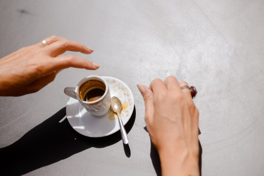 Šoljica sa espreso, ženske ruke, vidi se malo kafe prosute u tacnu. Sa starne na tacni je kašičica.