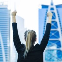 zena stoji okrenuta ka gradu u odelu sa podignutim rukama