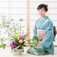 Žena u kimonu sedi pored cveća