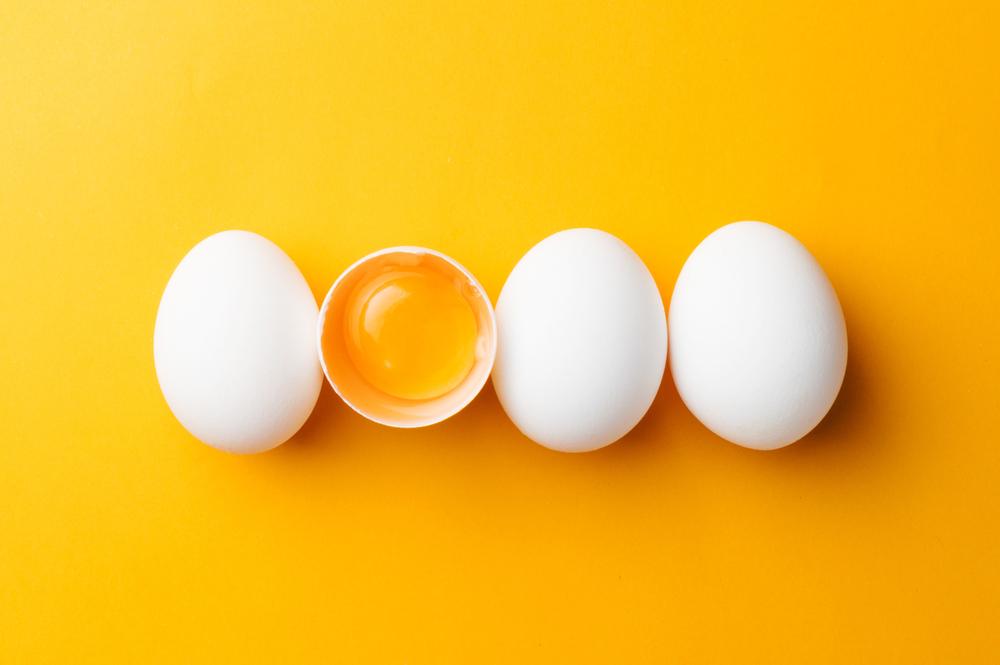 Četiri jaja na poređana u redu na žutoj podlozi. Jedno od jaja je prepolovljeno i vidi se žumance.
