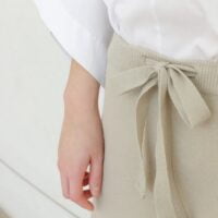 Bela košulja i bež pantalone koje imaju pojas u istoj boji vezan u mašnu.