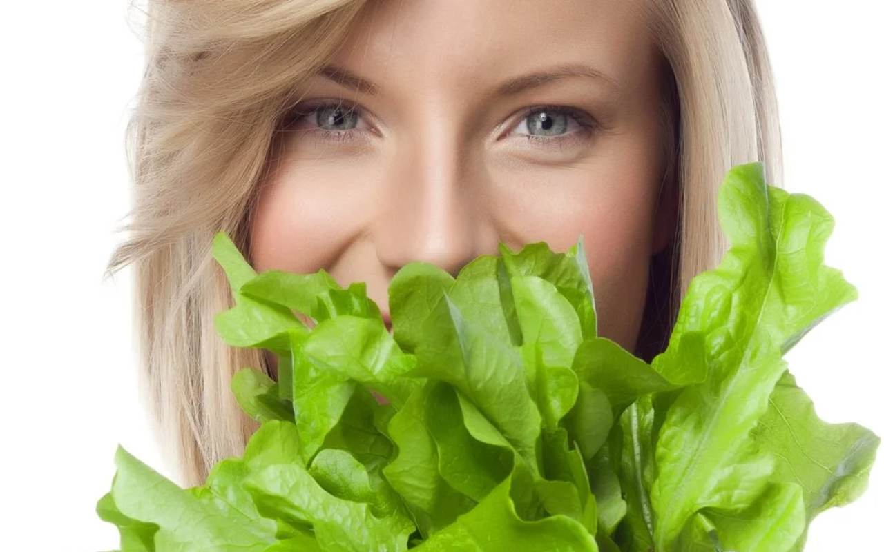 Žena koja drži svežu zelenu salatu ispred lica.