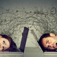 Mladić i devojka, sede za radnim stolom i drže spuštene glave na tastaturu sopstvenog lap topa zbog stresa