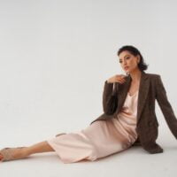 Devojka u bež satenskom kombinezonu, slip haljini. Preko ima sako.