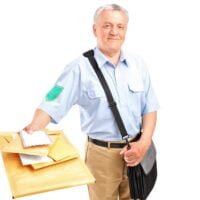 Poštar, sa torbom preko ramena, drži poismene pošiljke u desnoj rci