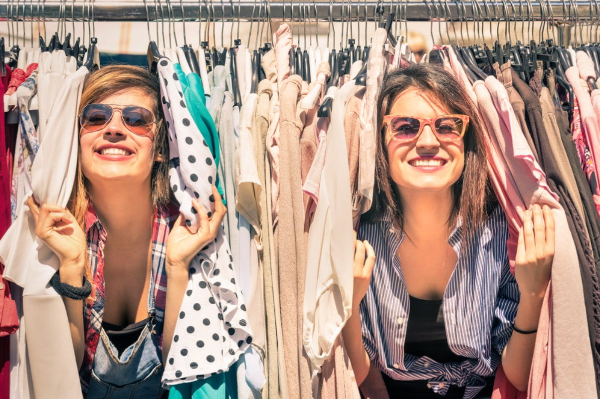 Dv devojke , s anaočarima za sunce, izviruju iz štendera sa second hand garderobom