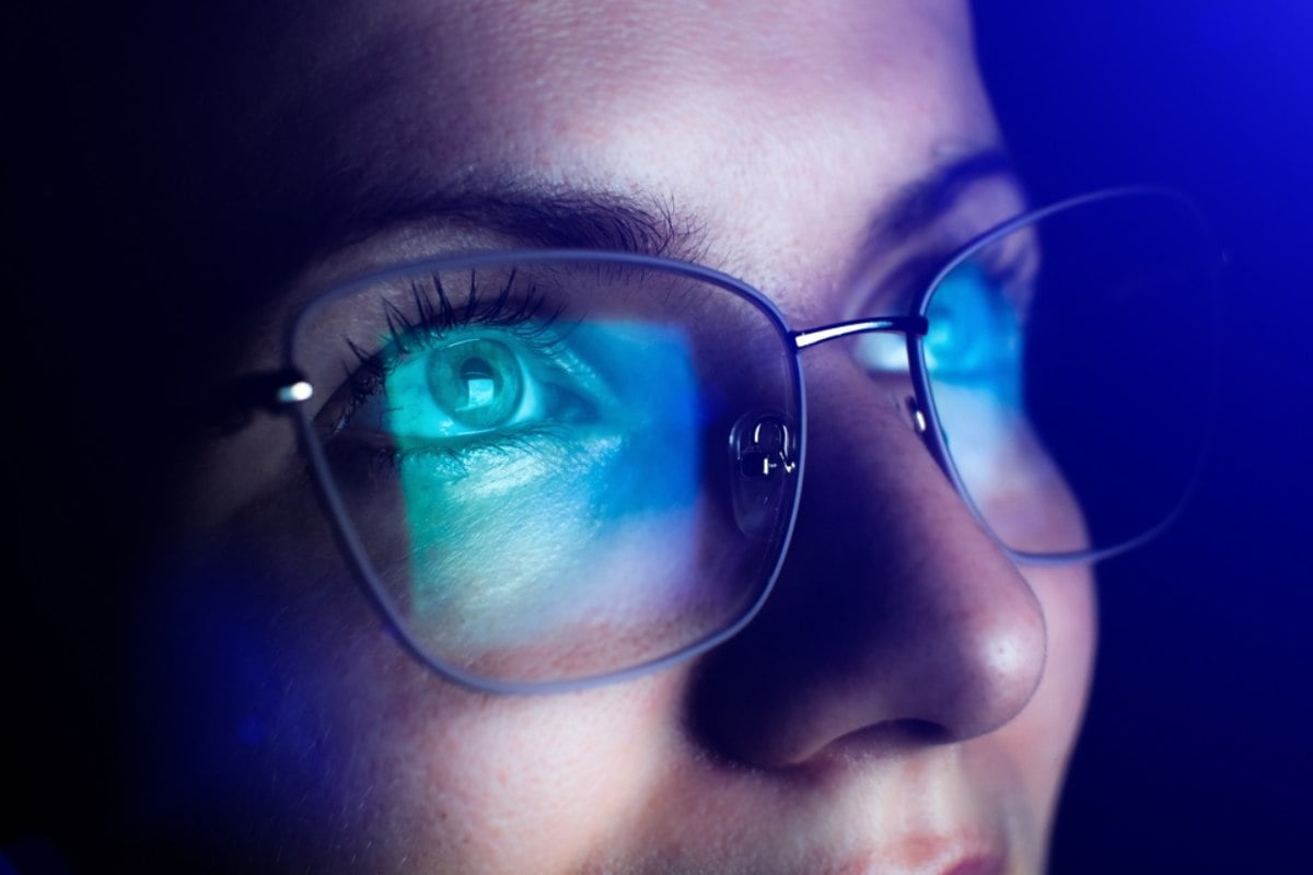 Žena koja u relativno tamnoj prostoriji očigledno gleda u kompjuter i na staklima njenih naočara se vidi refleksija plavog svetla.
