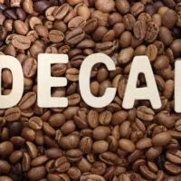 Veliki natpis, skraćenica DECAF, preko slike gomile zrna kafe