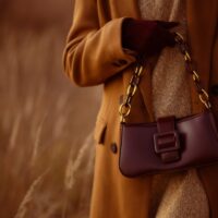 Žena u kaputu boje duvana, sa bordo tašnicom i rukavicama