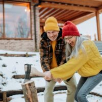 Muž pokazuje ženi kako se cepaju deva, napolju je sneg u pozadini je ognjište i kuća.