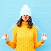 Devojka sa belom kapuom navučenom preko očiju, šalje poljubac crvenim usnama