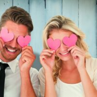 Zaljubljeni par sa roze srcima (isečenim od papira9, preko očiju, zaljubljeni.
