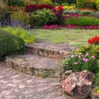 Vrt, u sredini su popločane stepenice i staza, sa strane je žbunasto cveće, a u pozadini travnjak.