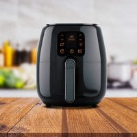 Air fryer na radnoj površini u kuhinju. U pozadini se nazire povrće.
