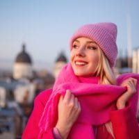 Vesela devojka u ružičastom džemperu, nosi beanie kapu.