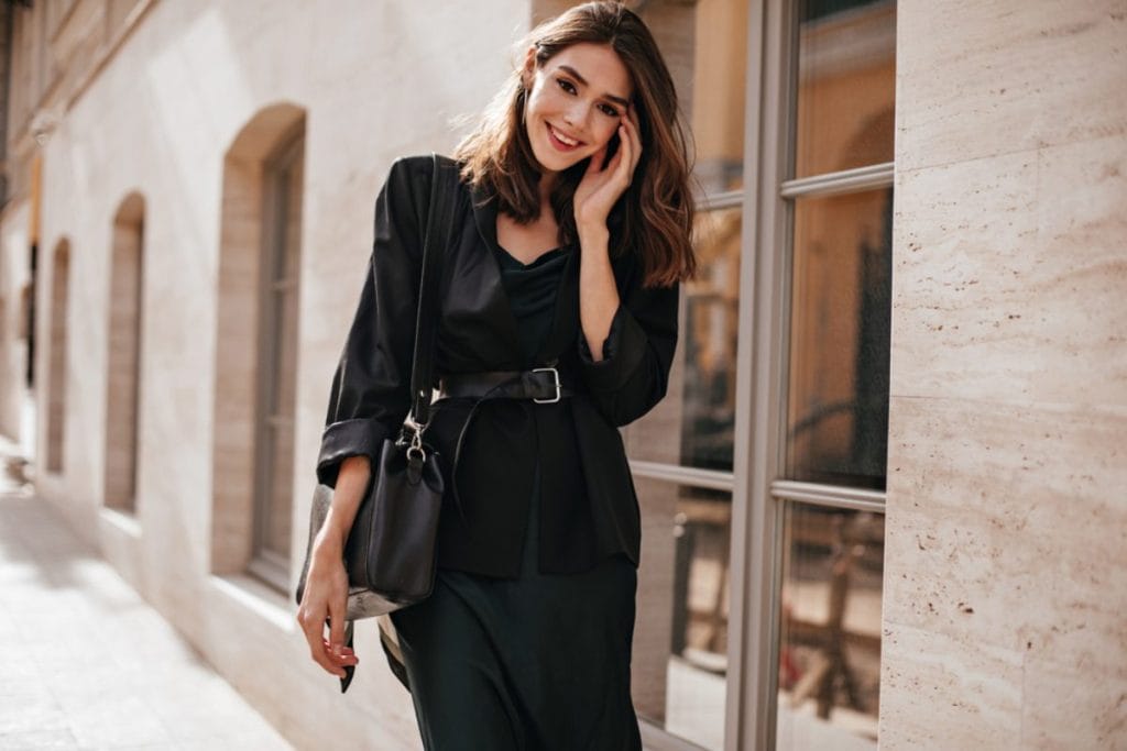 Nasmejana devojka u crnoj svilenoj haljini i crnim sakoom.