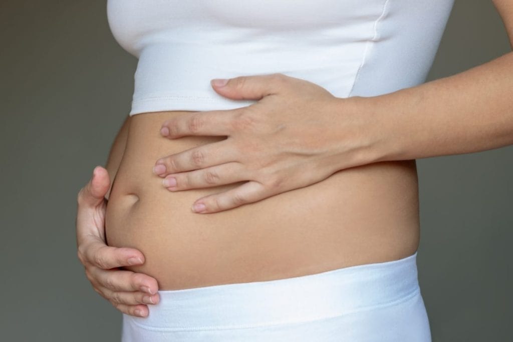 Žena, nadut stomak, drži ruke na stomaku.