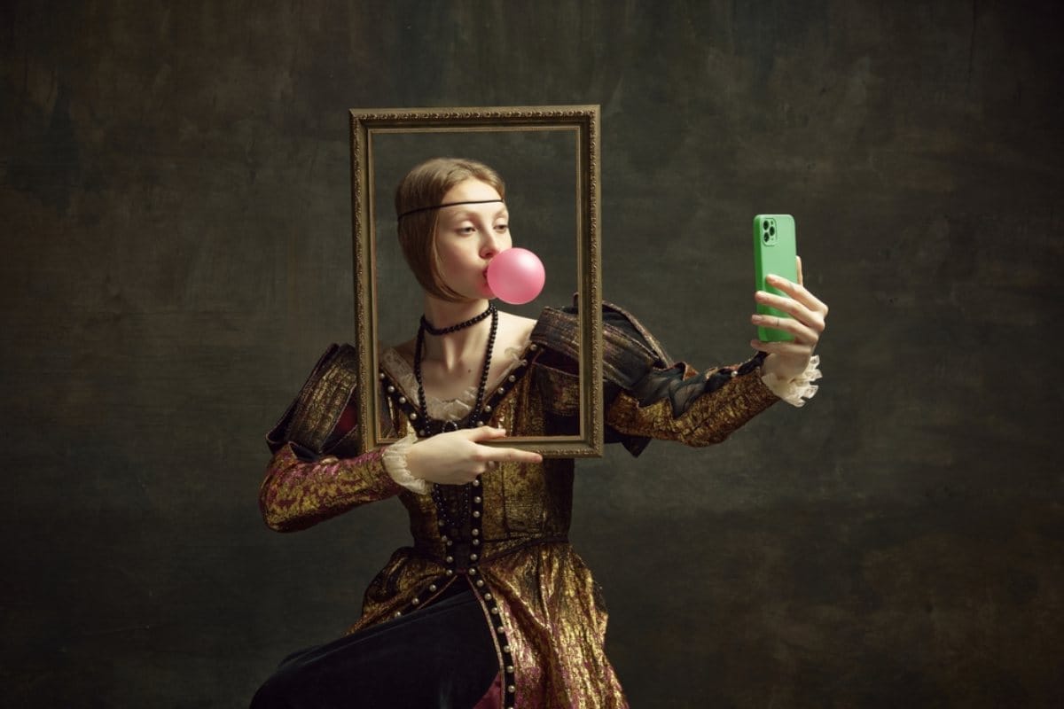 Žena u raskošnoj haljini iz prošlih vremena, drži ram ispred sebe, napravila je balon od žvake i slika selfie.