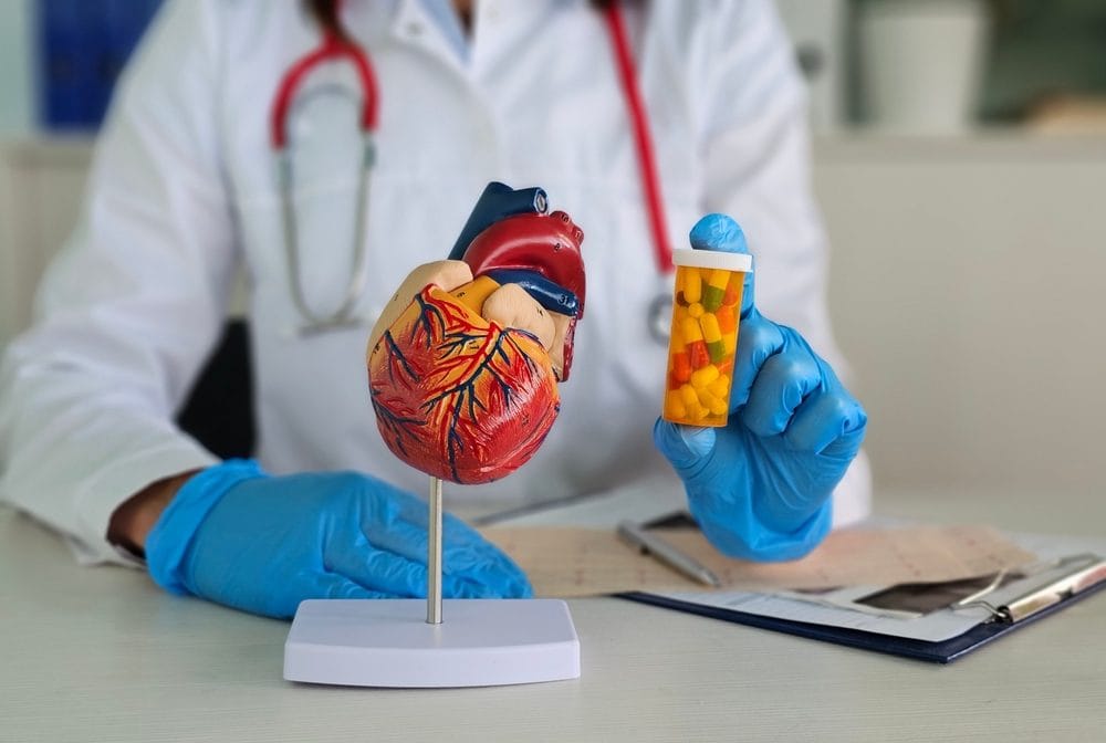 U lekarskoj ordinaciji, na stolu je model srca. Doktor u ruci drži kutiju sa lekovima.