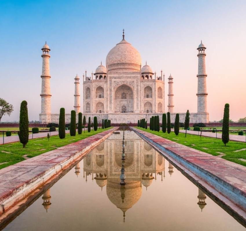 Taj Mahal, koji se ogleda u vodi ispred, okružen parkom.