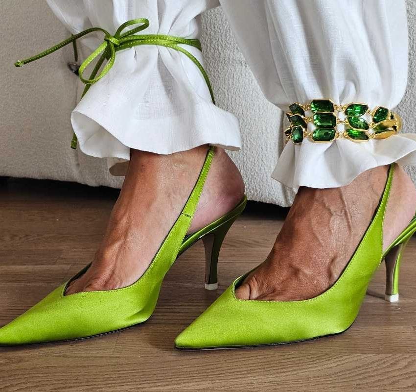 Nogavice belih pantalona su pritegnute oko gležnjeva, leva zelenom kožnom vrpcom, a desna zlatnim lancem na kome su smaragdno zeleni kristali.