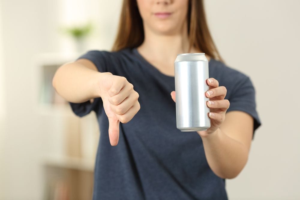 Devojka koja u jednoj ruci drži limenku sa energetskim pićem, a drugom rukom pokazuje palac na dole.