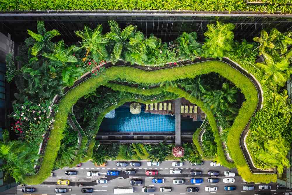 Hotel u Singapuru, okružen, odnosno sa svih strana oivičen džunglom, slikano iz vazduha, a dole ispred hotel vidi se prometna ulica sa puno automobila u nekoliko traka.