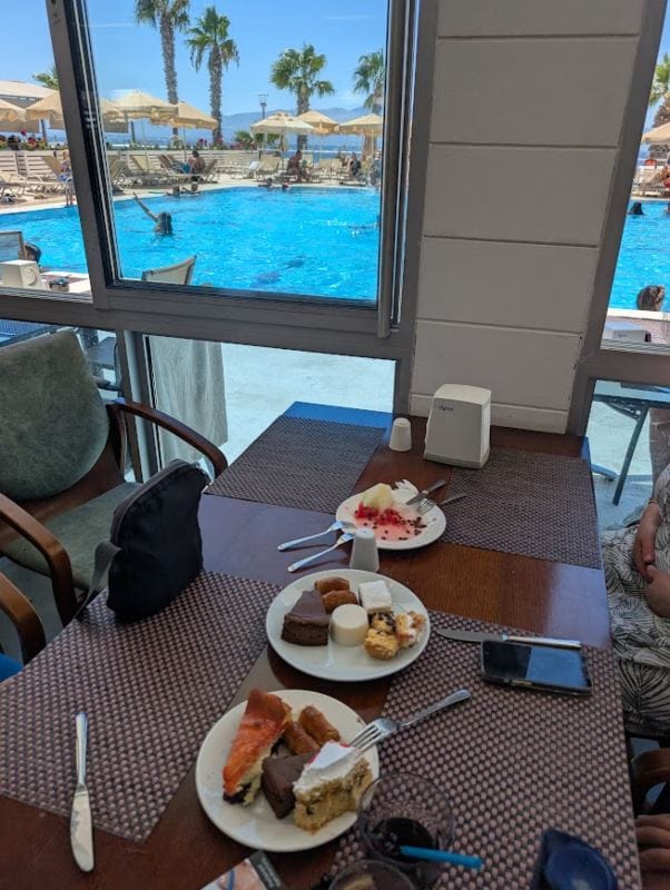 Kroz prozor se vidi bazen u resort-u, a na stolu su tanjiri sa nekoliko porcija kolača.