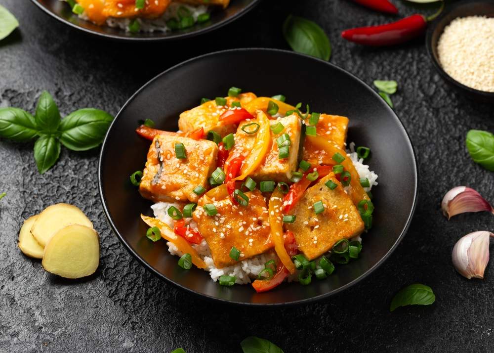 U crnoj ovalnoj činiji je obrok pripremljen sa tofuom i batatom. Servirano na pirinču.