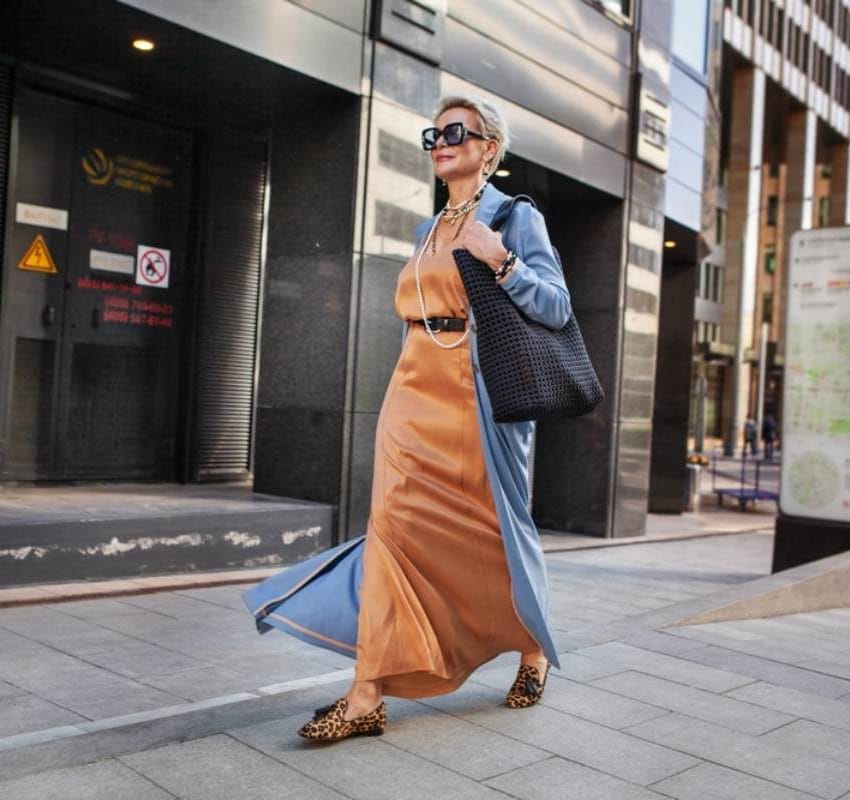 Žena koja ide na posao, ima maxi lanenu haljinu boje terakote, plavi ogrtač i veliku tašnu koju nosi preko ramena.