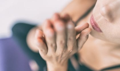 Žena koja meditire, drži ruke sklopljene ispred usta, praktikuje mantru ili hmmmm zujanje.