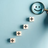 Kockice sa iscrtanim znakom plus, pore]anje jedna iznad druge, na vrhu je emoticon osmeh koji osoba posmatra kroz lupu.
