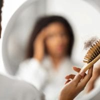 U ogledalu se vidi zamućena slika žene koja u ruci drži četku za kosu nakojoj je puno opalih dlaka.