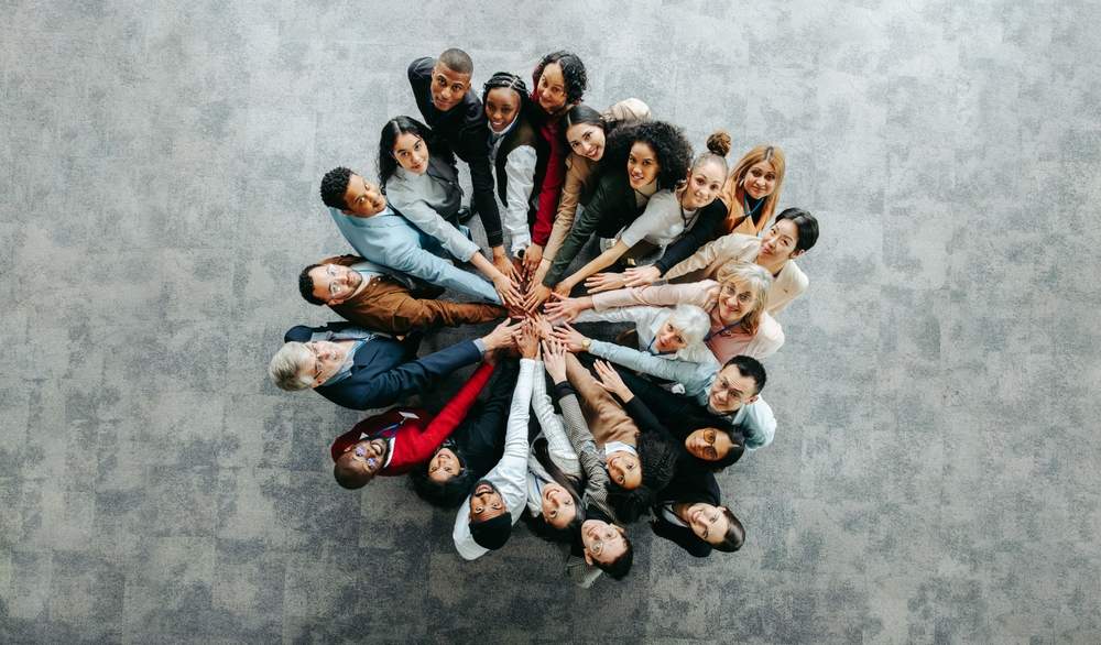 Grupa zaposlenih slikana odozgo, stoje u krugu i svi su pružili ruke ka centru.