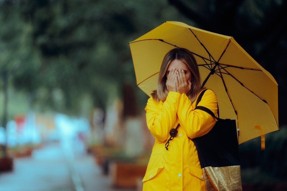 Tužna žena na kiši, drži žuti kišobran.