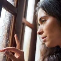 Tužna žena gleda kroz prozor, napolju pada kiša.