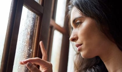 Tužna žena gleda kroz prozor, napolju pada kiša.