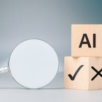 Dva kocke, na jednoj piše AI, a na donjoj kocki, na jednoj strani štrikla, a na drugoj znak za netačno. Pored je lupa.