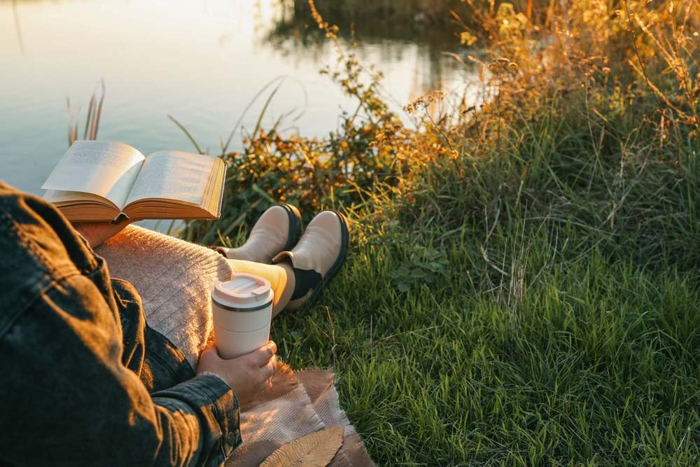 Žena koja sedi na obali jezera u jesen i čita knjigu.