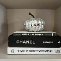 Knjige na polici. Na njih je postavljena bundeva obložena srebrnkastim samolepljivim listićima.