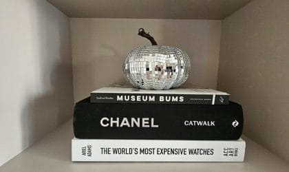 Knjige na polici. Na njih je postavljena bundeva obložena srebrnkastim samolepljivim listićima.