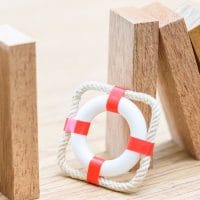 Drvene kocke koje se ruše, a pored stoji model pojasa za spasavanje. Figurativna ilustracija.