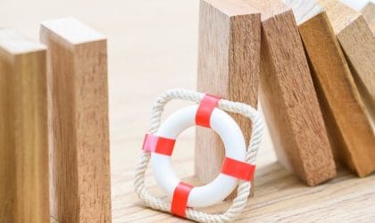 Drvene kocke koje se ruše, a pored stoji model pojasa za spasavanje. Figurativna ilustracija.